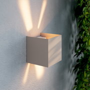 Moderne LED-Wandleuchte in kubischer Form, seitliche Perspektive, mit warmem Lichtstrahl nach oben und unten an einer strukturierten Wand.