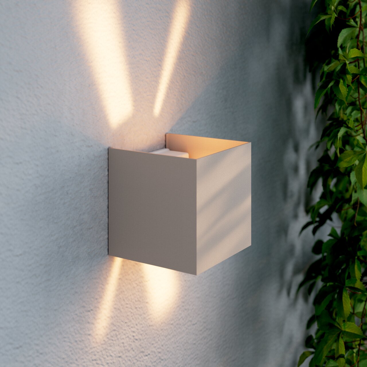 Moderne LED-Wandleuchte in kubischer Form, seitliche Perspektive, mit warmem Lichtstrahl nach oben und unten an einer strukturierten Wand.