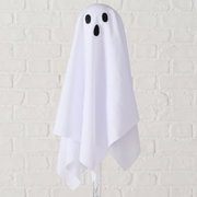 Weißes Halloween-Geister-Dekoelement mit schwarzem Augen- und Mundmotiv, frontal aus der Vorderansicht fotografiert vor heller Ziegelwand
