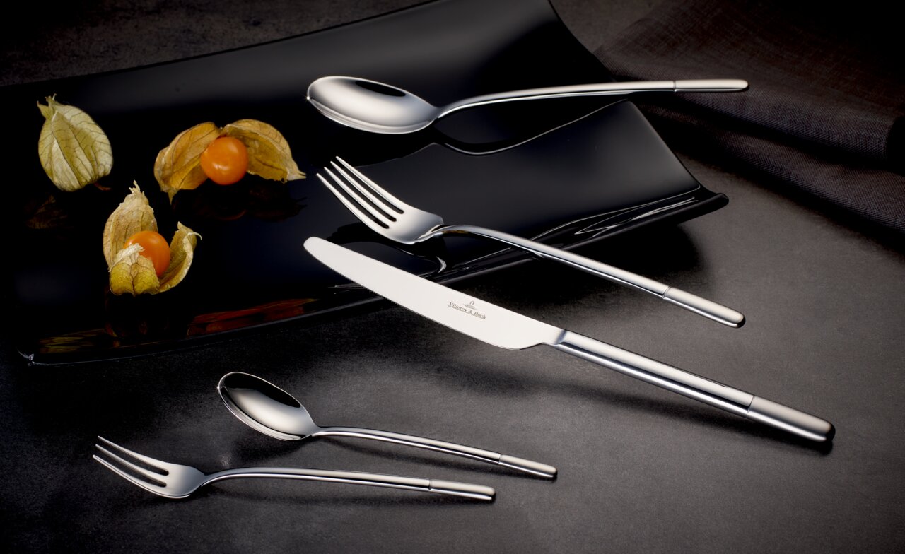 Elegantes, satiniertes 30-teiliges Besteckset auf schwarzem Teller mit Physalis, seitliche Perspektive.