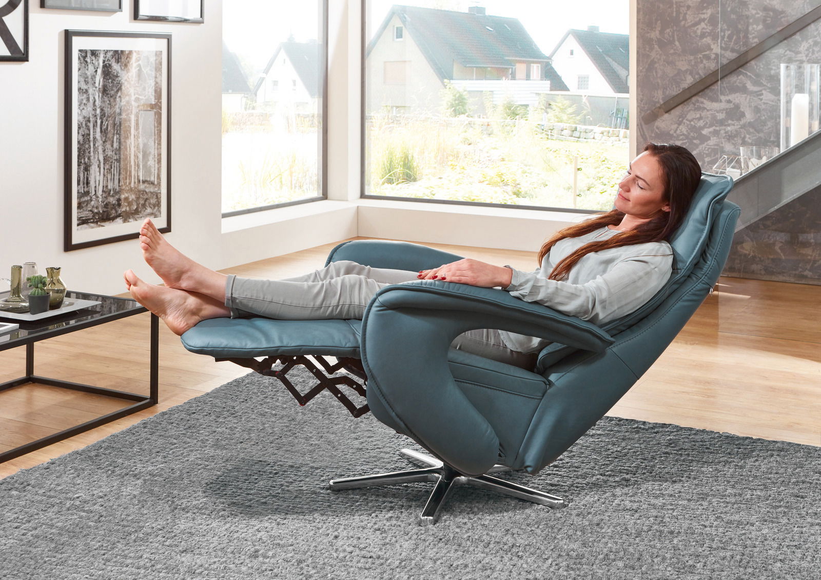 Frau entspannt in einem blauen Relax-Sessel Valdera mit hochgelegten Füßen, seitliche Perspektive.