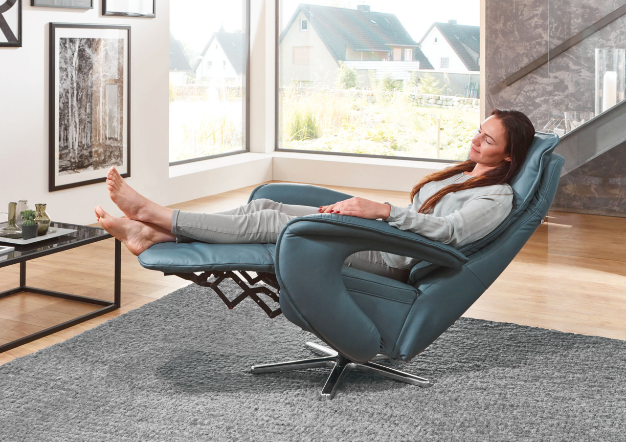Frau entspannt in einem blauen Relax-Sessel Valdera mit hochgelegten Füßen, seitliche Perspektive.