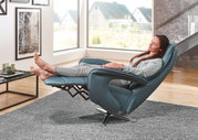 Frau entspannt in einem blauen Relax-Sessel Valdera mit hochgelegten Füßen, seitliche Perspektive.