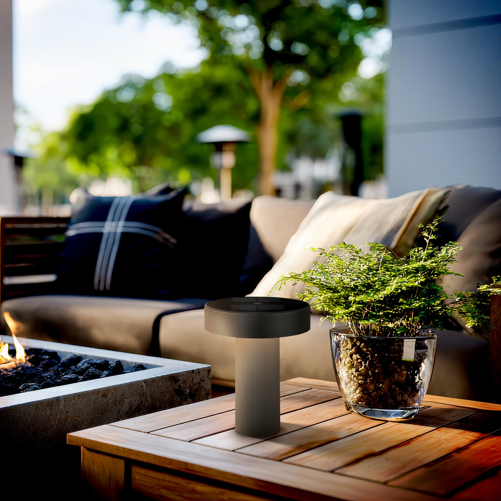 Moderne zwarte buitentafellamp op een houten tafel naast een glazen plantenbak op een loungeterras, in perspectief vanuit een laag, licht zijdelings vooraanzicht