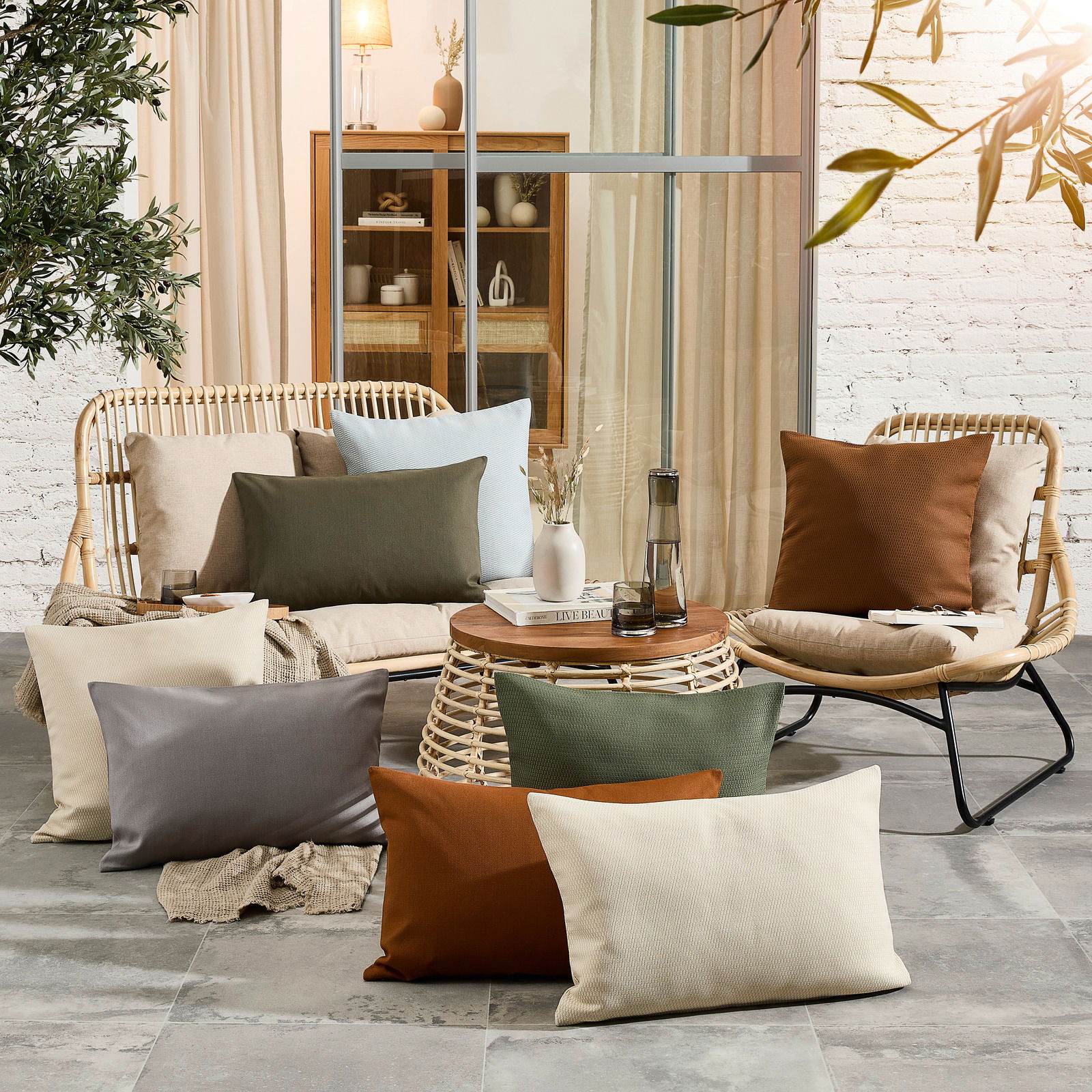 Outdoor-Kissenhüllen in verschiedenen Farben auf einer stilvollen Terrasse mit Rattanmöbeln, aus der Perspektive eines Betrachters, der die gemütliche Atmosphäre genießt.