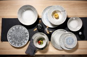 Verschillende dinerborden in diverse uitvoeringen en maten, van bovenaf gefotografeerd op een tafel met een donker tafelkleed.