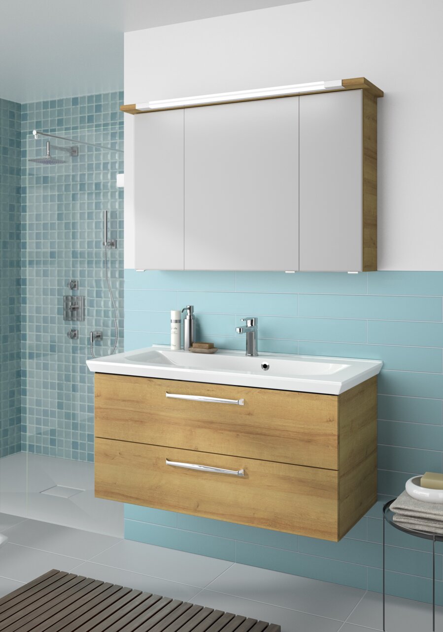Modern badkamermeubel met houtlook en een witte wastafel, gezien vanaf de voorkant, tegen een muur met blauwe tegels.
