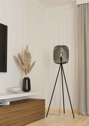 Moderne Stehleuchte ROMAZZINA mit schwarzem, dreibeinigem Gestell und offenem Lampenschirm aus Metallstreben, seitliche Perspektive im Wohnzimmer.