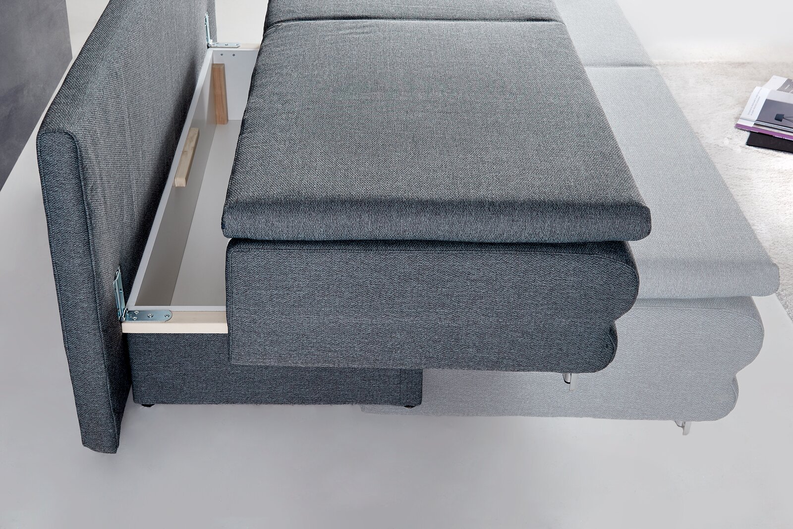 Querschläfer-Sofa in grauem Stoff, seitliche Perspektive mit ausgezogenem Bettkasten.