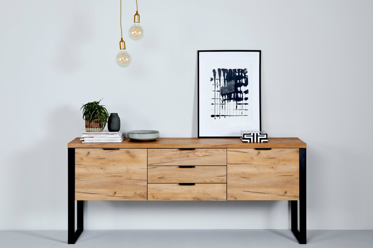 Modernes Sideboard aus Holz mit schwarzem Metallrahmen, dekoriert mit Pflanzen, Büchern und Kunstobjekten, aus frontaler Perspektive fotografiert.