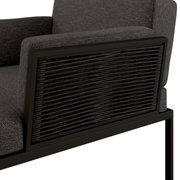 Detailfoto van een loungestoel met grijze stoffen bekleding en gevlochten zijkanten.