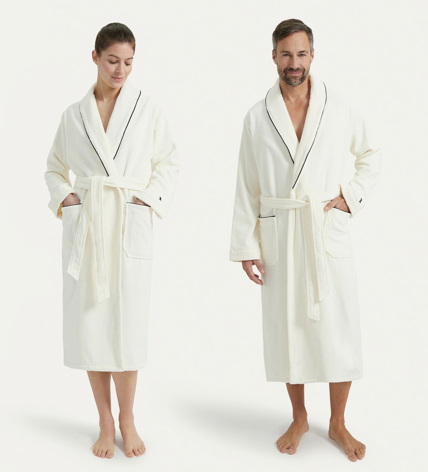 Zwei Personen tragen weiße Bademäntel mit Schalkragen und schwarzer Paspelierung, frontal fotografiert.