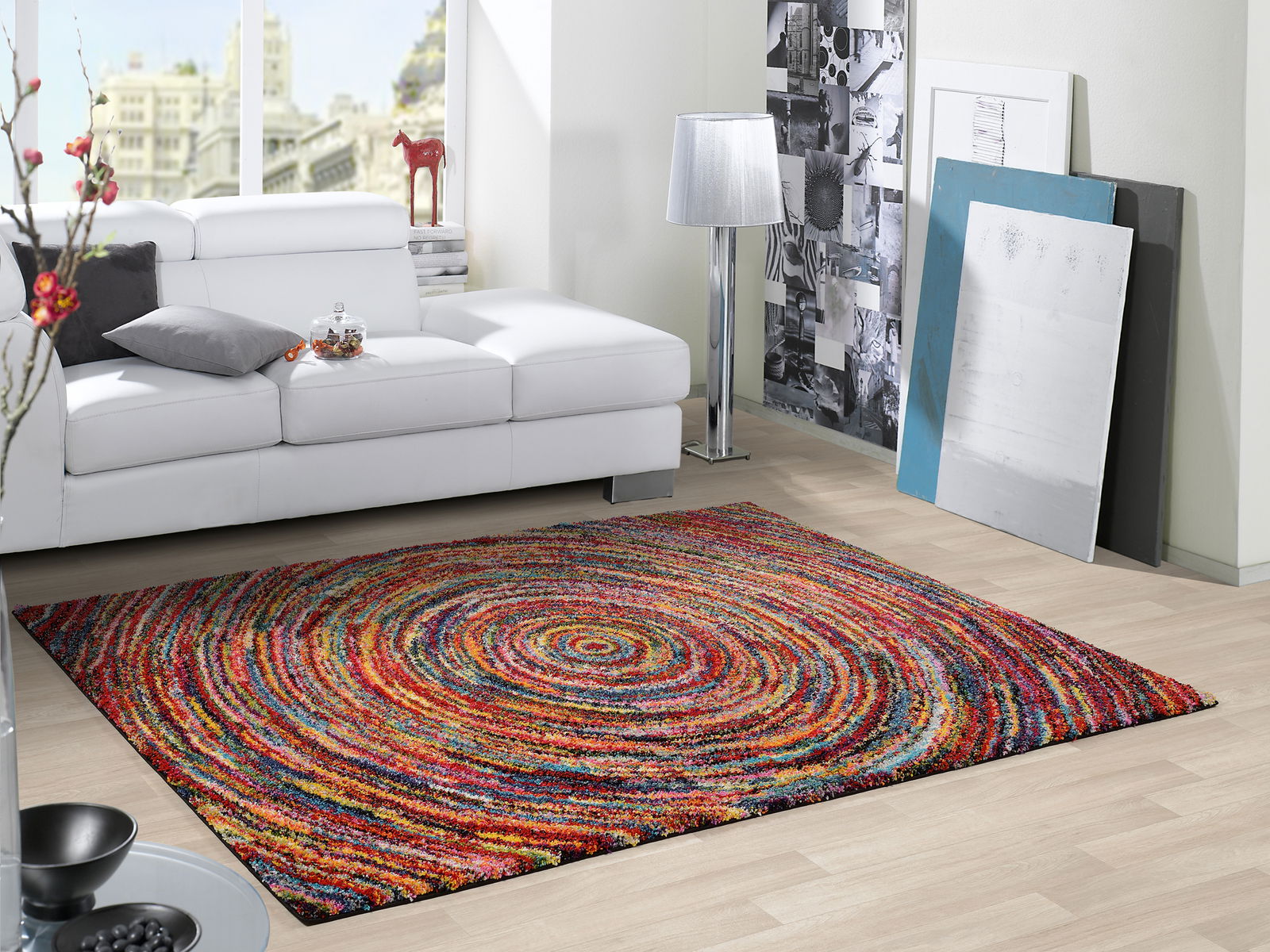 Hochflor-Teppich mit buntem, spiralförmigem Muster in einem modernen Wohnzimmer mit weißem Sofa, aus der Vogelperspektive betrachtet.