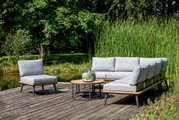 Moderne Outdoor-Lounge-Möbel auf einer Holzterrasse mit Blick auf einen Teich, bestehend aus einem Loungesessel, einer Loungebank und einem Loungetisch, umgeben von grüner Natur.