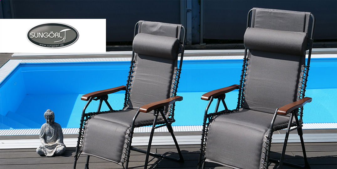 Zwei graue Relaxliegen mit Holzarmlehnen am Pool.