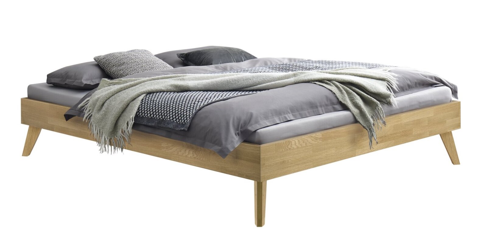 Modern houten bedframe in eikenlook met schuine poten, bekleed met grijs beddengoed en een deken, schuin vooraanzicht