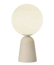 Moderne Tischleuchte mit kugelförmigem, weißem Lampenschirm und konischem, steinfarbenem Sockel, frontal abgebildet.