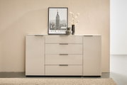 Moderne weiße Hochglanz-Kommode/Sideboard mit zwei Türen und vier mittigen Schubladen, schwarzen Griffleisten und Deko (New-York-Poster, Vasen mit Zweigen) auf der Oberfläche, frontal aus leicht erhöhter Perspektive fotografiert