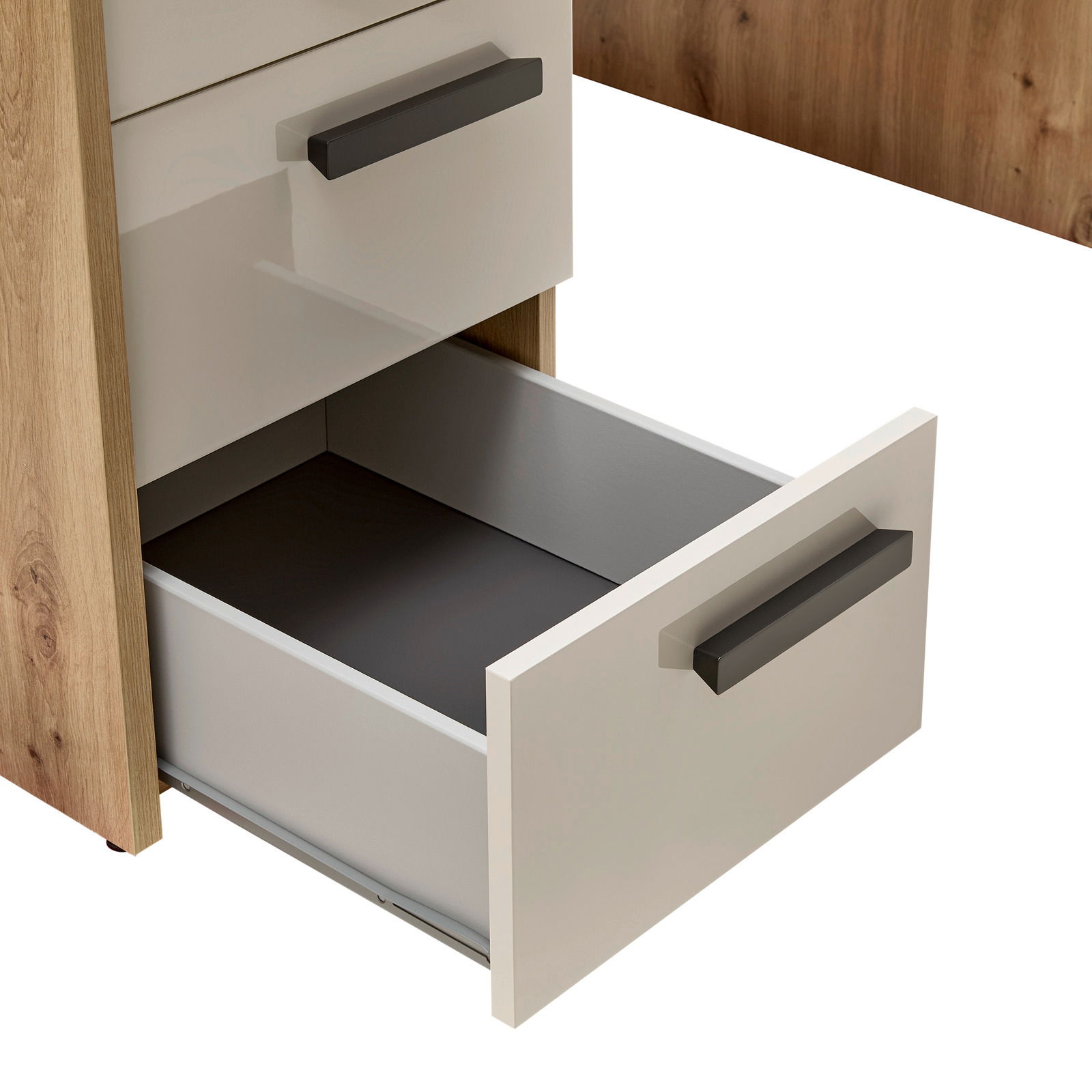 Nahaufnahme eines Schreibtischs mit geöffneter Schublade, Holzoptik mit weißen Fronten und schwarzen Griffen, seitliche Perspektive.
