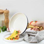 Eine Hand hält eine Pfanne mit goldfarbenem Griff, aus der ein Omelett mit Paprika und Kräutern auf einen Teller gleitet. Perspektive von der Seite.