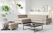 Modernes beiges L-förmiges Ecksofa mit gepolsterter Rückenlehne und passendem Hocker in hellem Wohnzimmer, Perspektive: frontale 3/4-Ansicht von leicht links.