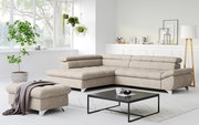 Modernes beiges L-förmiges Ecksofa mit gepolsterter Rückenlehne und passendem Hocker in hellem Wohnzimmer, Perspektive: frontale 3/4-Ansicht von leicht links.