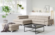 Modernes beiges L-förmiges Ecksofa mit gepolsterter Rückenlehne und passendem Hocker in hellem Wohnzimmer, Perspektive: frontale 3/4-Ansicht von leicht links.