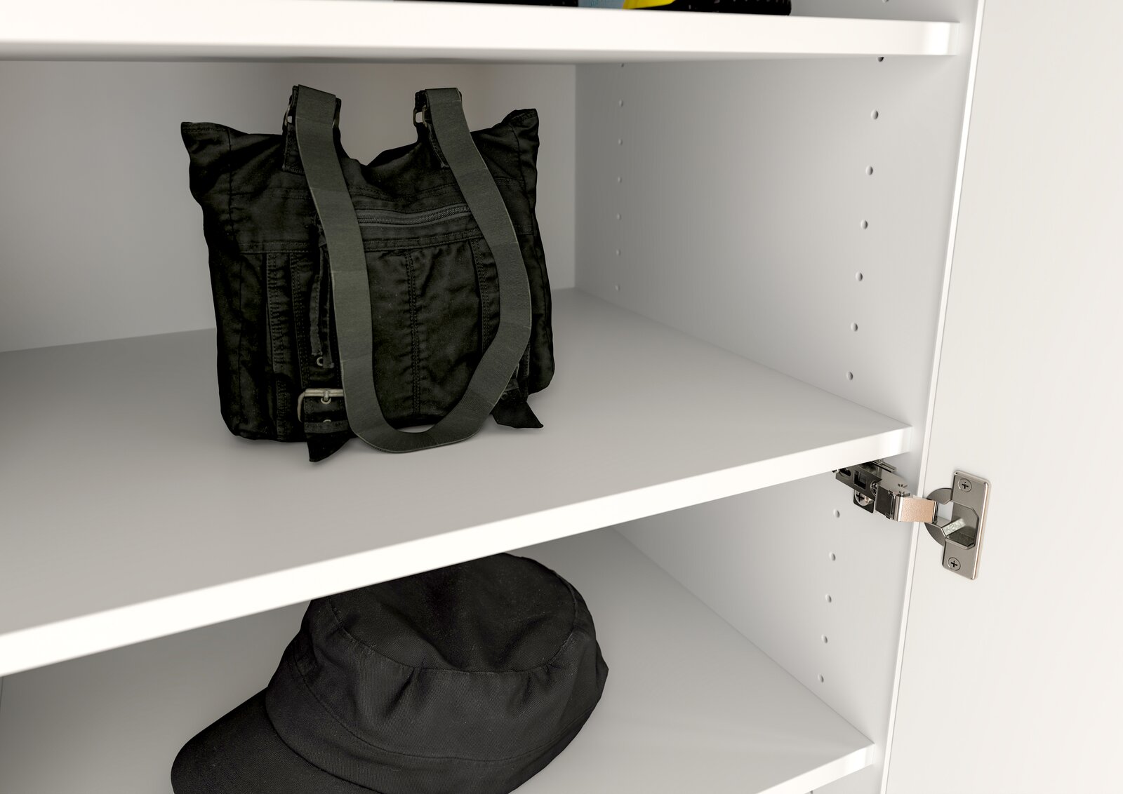 Innenansicht eines weißen Garderobenschranks mit zwei Regalböden, auf denen eine schwarze Tasche und ein schwarzer Hut liegen. Perspektive von schräg vorne.
