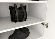 Innenansicht eines weißen Garderobenschranks mit zwei Regalböden, auf denen eine schwarze Tasche und ein schwarzer Hut liegen. Perspektive von schräg vorne.