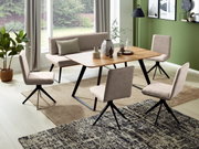 Eetkamer met een moderne tafel en bank in houtlook, omringd door vier gestoffeerde stoelen, gezien vanuit de kamer met uitzicht op grote ramen en een groene muur.