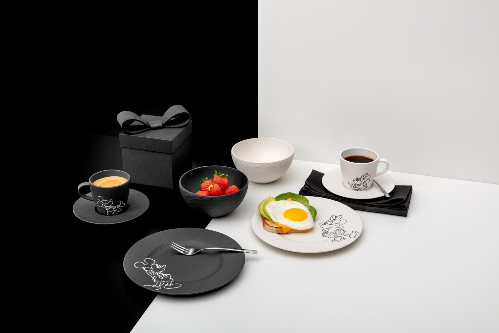 Villeroy & Boch Ontbijtset 8-delig MICKEY MOUSE Zwart-witte ontbijtset met kopjes, borden en schalen met een cartoonmotief, gedekt met koffie, aardbeien en toast met een spiegelei op een tweekleurige achtergrond, gezien schuin van voren/bovenaf.