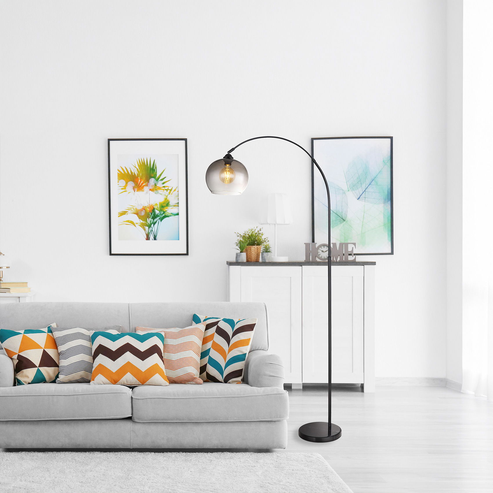 Modernes Wohnzimmer mit grauem Sofa, bunten Kissen, Bogen-Stehlampe und zwei Bildern an weißer Wand