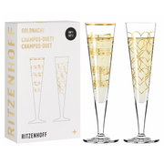 Zwei elegante Champagnergläser mit goldenen Verzierungen, eines mit Noten und das andere mit Herzmotiven, vor einer Verpackung mit der Aufschrift 'Ritzenhoff'. Frontalansicht.
