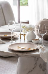 Elegante Tischdekoration mit beiger Schale NewMoon 750ml, goldfarbenem Besteck und Weingläsern auf einem Marmortisch, seitliche Perspektive.