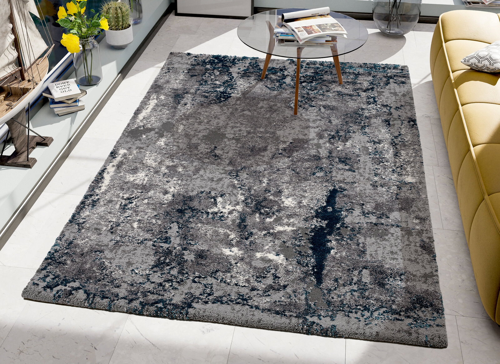 OCI Webteppich 200x290 cm JUWEL Moderner Teppich in Grau- und Blautönen, rechteckig, auf einem hellen Boden in einem stilvoll eingerichteten Raum mit gelbem Sofa und Glastisch, aus der Vogelperspektive betrachtet.