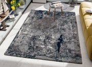 Moderner Teppich in Grau- und Blautönen, rechteckig, auf einem hellen Boden in einem stilvoll eingerichteten Raum mit gelbem Sofa und Glastisch, aus der Vogelperspektive betrachtet.