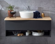 Moderner Waschtisch mit rundem weißen Waschbecken auf einer Holzplatte, dekoriert mit einer Pflanze, Seifenspender und Handtuch, frontal betrachtet.