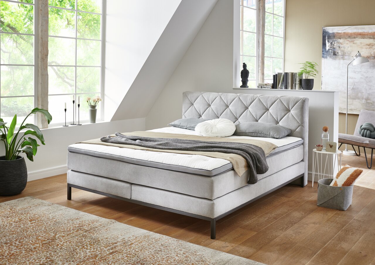 Modern boxspringbed in een lichte kamer met grote ramen, zijaanzicht