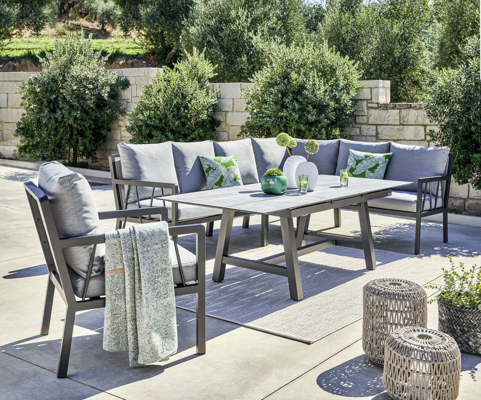 Amatio Lounge-Mittelteil ZAMORA Garten-Lounge-Set mit grauen Kissen und Tisch, umgeben von Pflanzen, aus seitlicher Perspektive fotografiert.