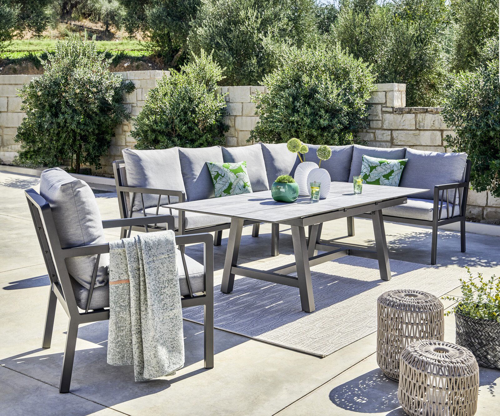 Amatio Lounge-Mittelteil ZAMORA Garten-Lounge-Set mit grauen Kissen und Tisch, umgeben von Pflanzen, aus seitlicher Perspektive fotografiert.