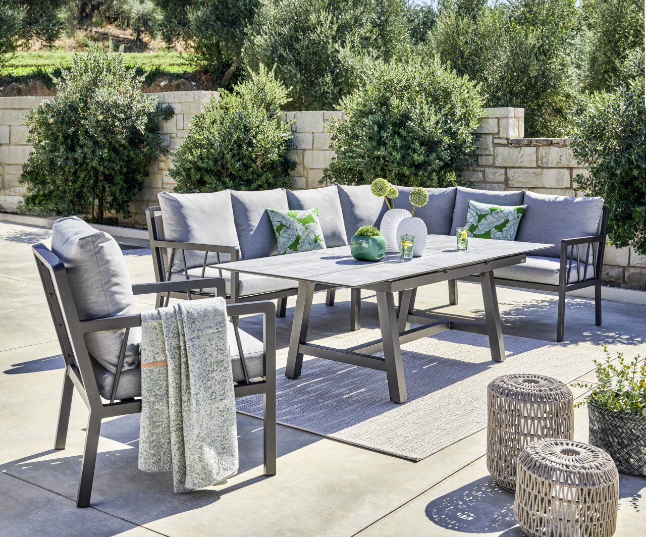 Amatio Lounge-Mittelteil ZAMORA Garten-Lounge-Set mit grauen Kissen und Tisch, umgeben von Pflanzen, aus seitlicher Perspektive fotografiert.