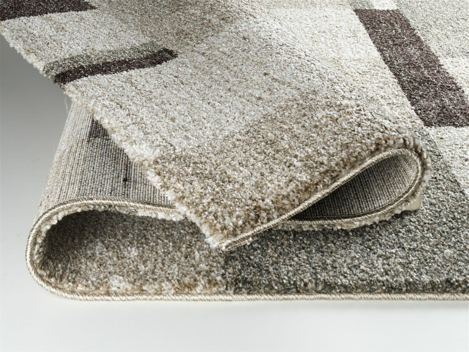 Nahaufnahme eines umgeschlagenen Teppichs mit geometrischem Muster in Beige- und Brauntönen, Perspektive von der Seite.