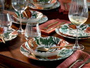 Gedeckter Holztisch mit floral gemustertem Porzellan-Geschirr, goldfarbenem Besteck, Gläsern und Weißweinglas, schräg von oben aus der Nähe fotografiert.
