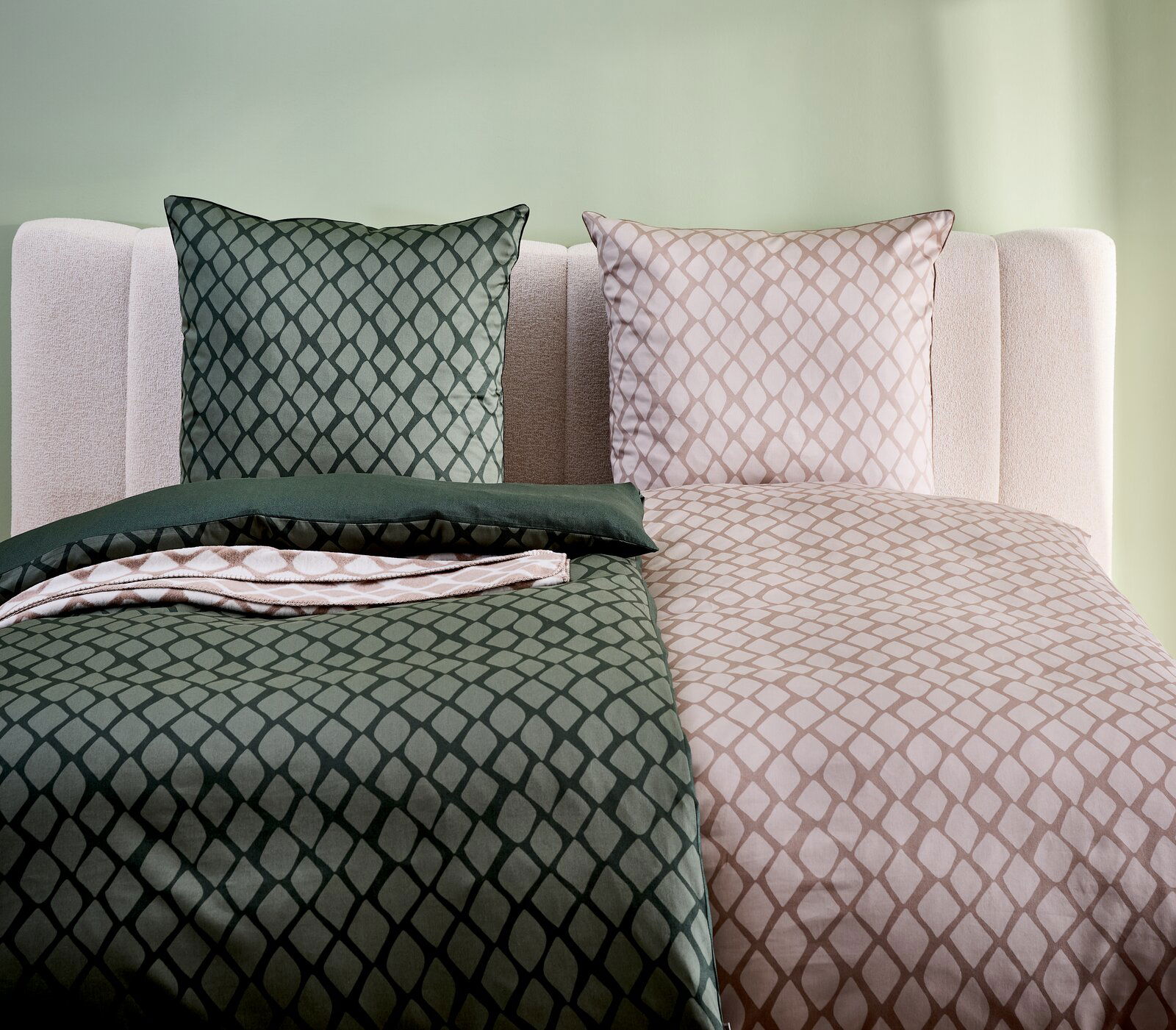 Wendebettwäsche in grünem und beigem Rautenmuster, auf einem Bett mit hellgrüner Wand im Hintergrund, aus der Vorderansicht fotografiert.
