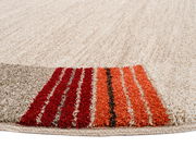 Nahaufnahme eines runden Frisé-Teppichs mit cremefarbenem Hintergrund und roten, orangen sowie braunen Streifen am Rand, aus seitlicher Perspektive fotografiert.