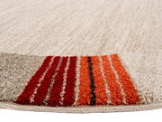 Nahaufnahme eines runden Frisé-Teppichs mit cremefarbenem Hintergrund und roten, orangen sowie braunen Streifen am Rand, aus seitlicher Perspektive fotografiert.