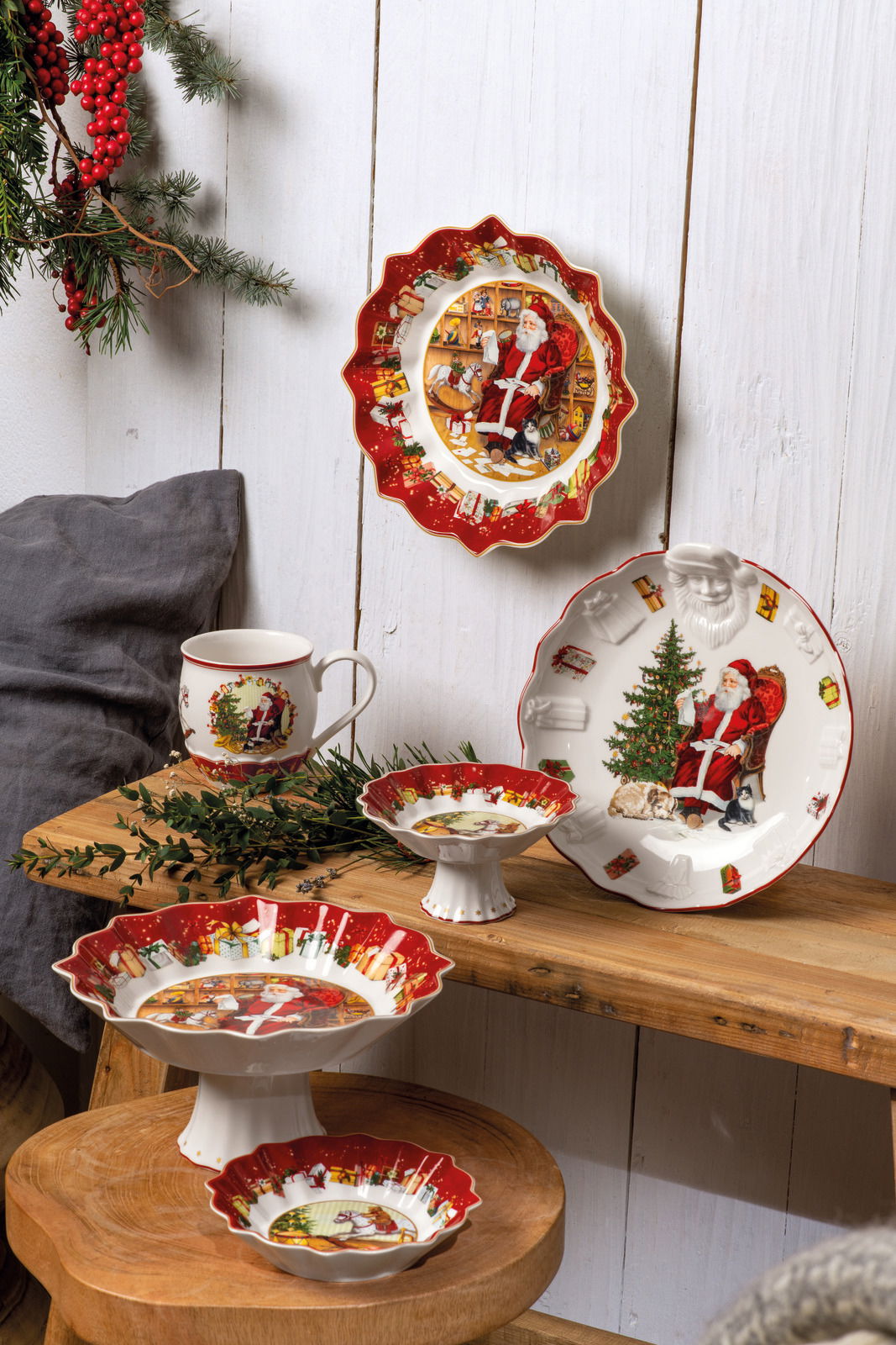 Weihnachtliche Geschirrkollektion mit kleinen Schalen und Tellern, verziert mit Weihnachtsmannmotiven, auf einem Holztisch arrangiert. Perspektive von vorne.