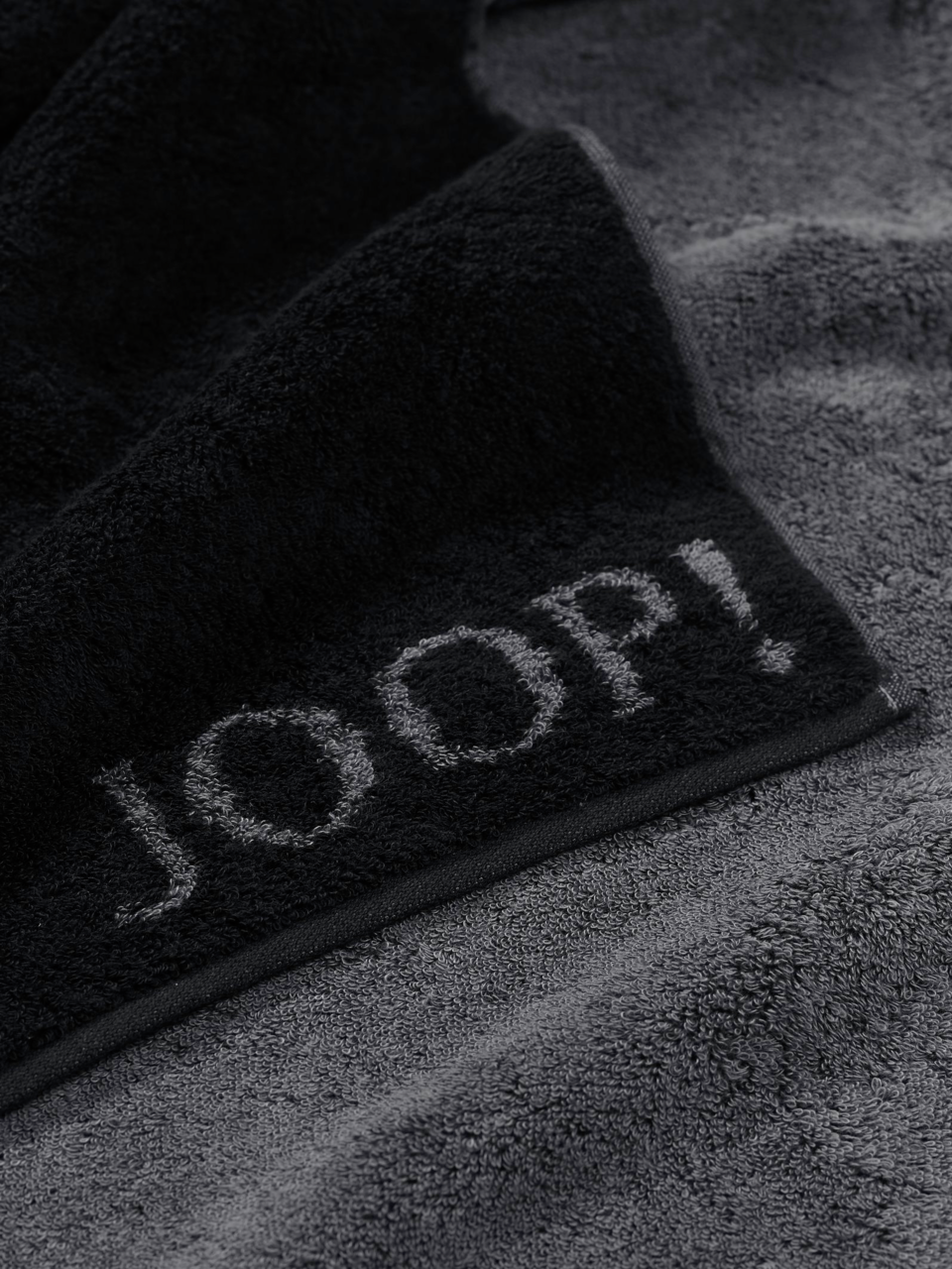 JOOP! Duschtuch 80x150 DOUBLEFACE CLASSIC Nahaufnahme eines grauen Duschtuchs mit dem Schriftzug 'JOOP!' in schwarzer Farbe.
