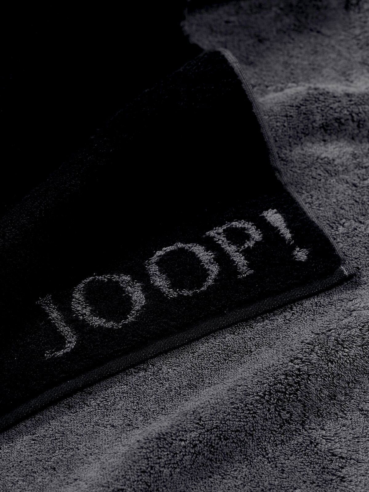JOOP! Duschtuch 80x150 DOUBLEFACE CLASSIC Nahaufnahme eines grauen Duschtuchs mit dem Schriftzug 'JOOP!' in schwarzer Farbe.