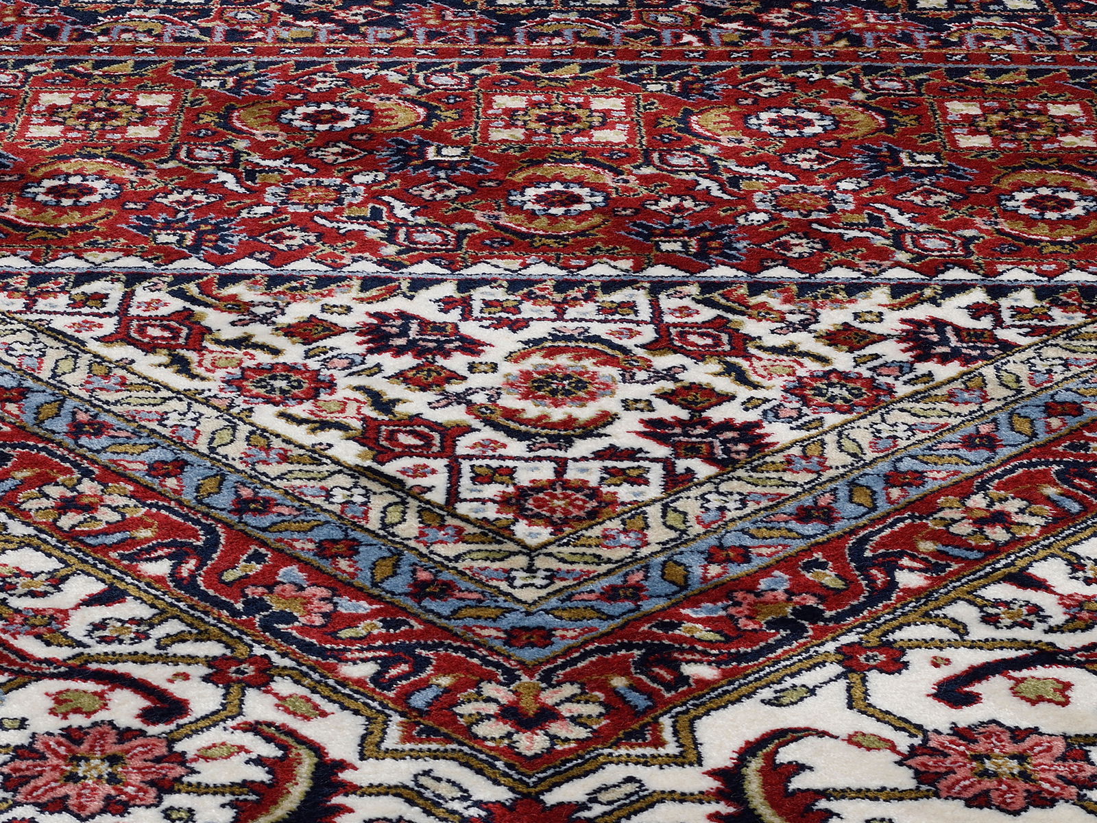 Nahaufnahme eines Orientteppichs mit komplexen, farbenfrohen Mustern in Rot, Blau und Weiß. Die Perspektive zeigt den Teppich schräg von der Seite.